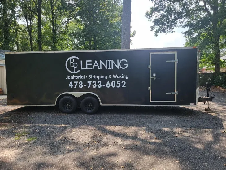 BP Cleaning's trailer with their logo and contact information on the side, parked in front of a house with a clean driveway and a well-kept lawn.